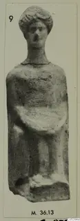 Small terracotta standing figure with curled hair and bent arms, shown on a mounted photograph.