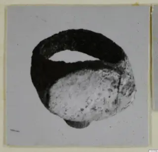 Silver ring with a dark, tarnished band and a pale rounded element, photographed on a grey card mount