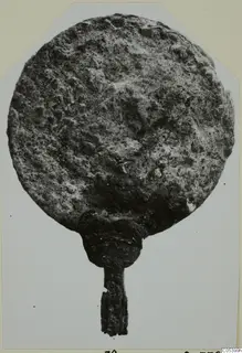 Corroded bronze disc with a short handle, from Marion tombs 61–98, photographed face-on on a mounted card.