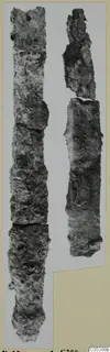 Two long, narrow, heavily corroded iron objects standing side by side on a photo mount