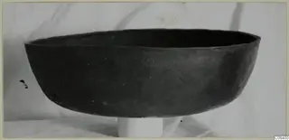 Dark wide bowl with a rounded body and everted rim, photographed in profile on a pale stand.