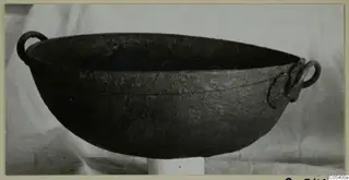 Dark bowl with two ring handles near the rim, shown in side view against a light cloth