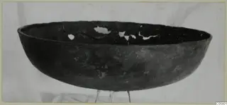 Dark, wide shallow bowl from Marion with holes broken in its upper wall, photographed on a wire stand