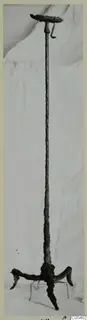 Corroded iron object with a flat disc top, long shaft and three curved feet, standing upright on white cloth