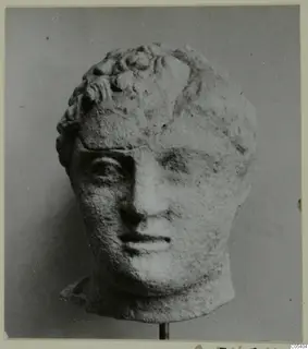 Sculpted head from Mersinaki with short curled hair, pale stone-like surface, mounted on a thin metal stand