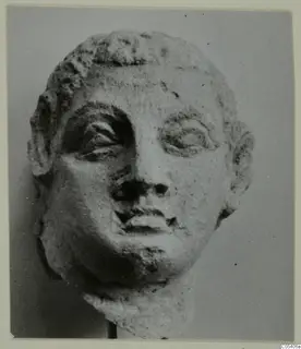 Sculpted head from Mersinaki with curled hair over the forehead, heavy-lidded eyes, prominent ears and a broken neck.