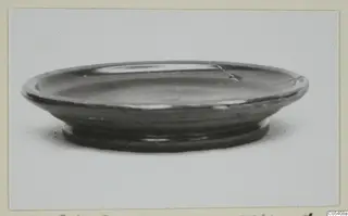 Shallow black-glazed bowl with a flaring rim and a ring foot, photographed from the side.