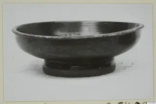 Black glazed bowl with a low ring foot, photographed in side view.