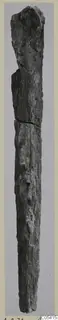 Long, narrow corroded iron dagger standing upright against a plain grey background