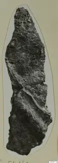 Corroded elongated find from Amathus tombs 2-26, cut out and mounted on a cream card