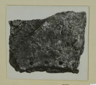 Fragment of a dark, encrusted object with three round holes along its lower edge, from Amathus tombs 2-26.