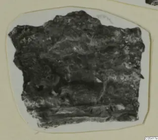 Dark, irregular fragment of an unidentified object from Amathus, photographed on a white card mount.
