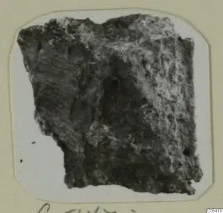 Dark, rough fragment from Amathus, tomb group 2-26, mounted on a white card with a handwritten label