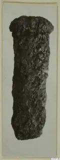 Corroded iron object, roughly cylindrical with a flared top end, photographed upright against a pale card.