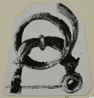Corroded metal object from Amathus, tomb 2-26, with a large loop and a ring-shaped end, photographed on a card mount