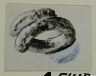 Silver ring from Marion Tomb 26, corroded, with a second band curving behind it, shown on a pale mounted card