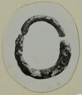 Dark, corroded open ring with a gap at the top, shown as a cut-out photograph on a cream card