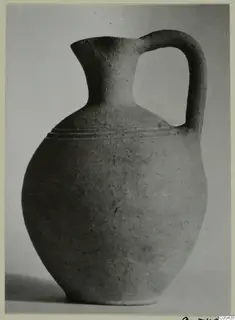 Plain pottery jug with a rounded body, a flared lip and a single strap handle, photographed on a grey surface.
