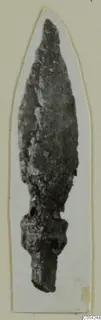 Corroded iron arrowhead with a pointed blade and tang, mounted on a white card