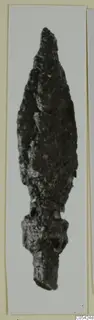 Corroded iron arrowhead with a long leaf-shaped blade and a socket, photographed on a pale card mount.