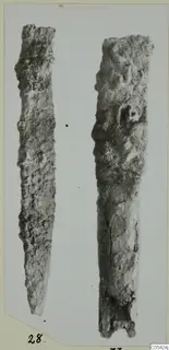 Two corroded iron tools, long and narrow, shown side by side on a pale mount.