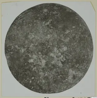 Round, corroded bronze disc from Marion, shown on a white card mount.