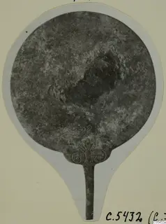 Bronze mirror with a long tang and an openwork palmette-and-scroll finial, from Marion Tomb 57.
