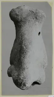 Limestone figurine: a headless, armless torso of pale stone, photographed against a grey background.