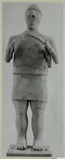 Terracotta Proto-Cypriote I statue of a standing figure with a cap and hands raised to the chest, on a rectangular base.