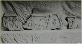 Three carved stone relief plaques with figures and animals, including a lion, set on a draped cloth.