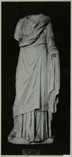 Headless draped marble statue of a standing figure, photographed against a dark background