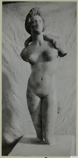 Marble statue of a standing nude female figure with the arms missing, set on a plinth.