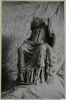 Headless marble sculpture of a seated, draped figure, photographed against a crumpled cloth backdrop