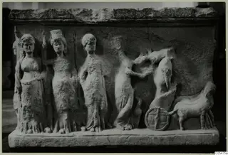 Carved stone relief block with standing draped female figures, a horse and a chariot wheel