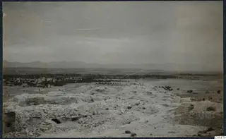 Excavated ground at Idalion with stone walls in the foreground, trees and a town beyond, and mountains on the horizon.