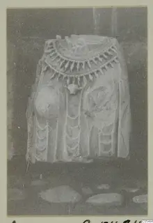 Carved stone statue fragment from Arsos with a broad pendant collar, photographed on a card mount