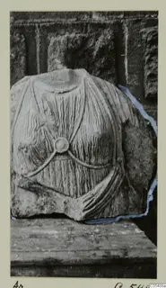Headless stone statue fragment from Arsos, a torso with pleated drapery and a round disc at the chest