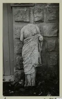 Headless stone statue of a draped female figure standing against a stone wall at Arsos.