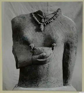 Headless limestone statue torso with a necklace, cross-hatched chest and one hand held at the waist.