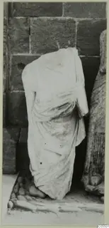 Headless draped marble statue standing against a wall of large stone blocks