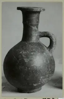 Red-slipped jug with a flared rim, single loop handle and round body, photographed against a grey backdrop.