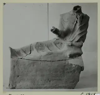 Terracotta figurine of a headless seated figure on a block base, one arm stretched forward