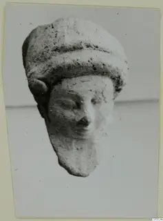 Terracotta figurine head with a tall banded headdress and a worn face, from Mersinaki