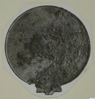 Round bronze plaque from Tomb 25 at Marion, corroded, mounted on a white octagonal card