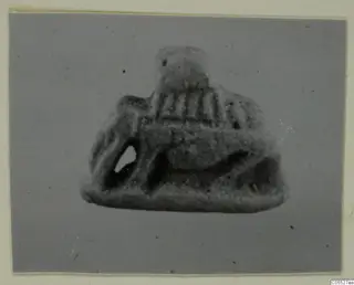 Small grey object from Amathus with a rounded top, vertical grooves and a pierced opening, photographed on a grey backdrop