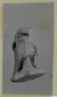 Small figurine with a squared head and broad flat base, shown in a photograph on a grey card mount