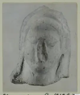 Front view of a fragmentary terracotta figurine face, the broken lower edge visible
