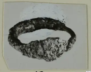 Silver ring with a corroded, pitted surface and a break in its lower part, shown on a mounted print