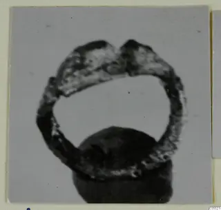 Silver ring with a broad hoop and raised shoulders at the top, photographed standing on a dark rounded base.