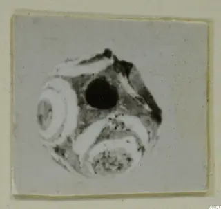 Round bead-like object with a large dark hole, from Marion, Tomb 26, shown on a card mount